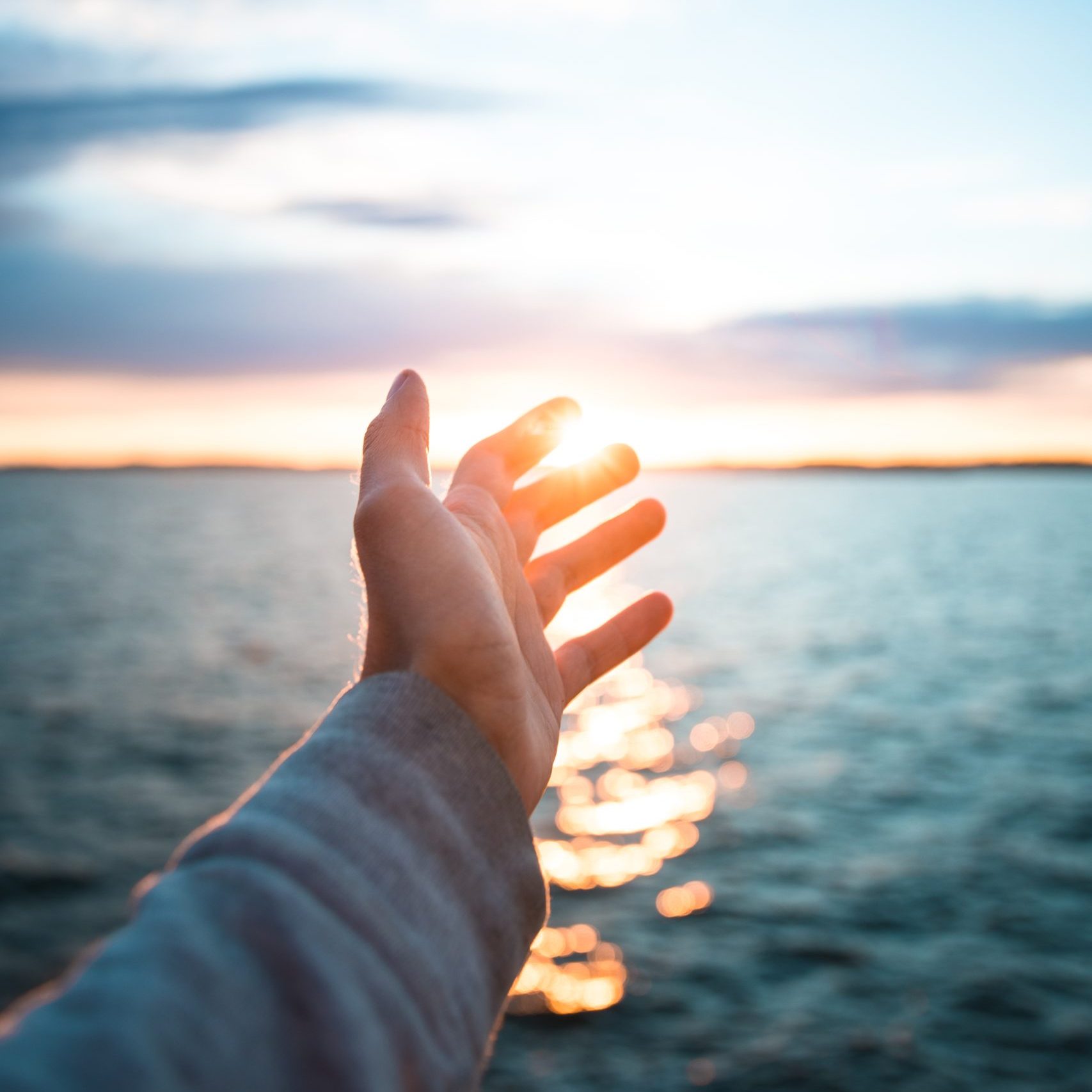 A vertical shot of a hand with the beautiful sea in the background during suns